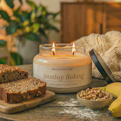 Candle labeled 'Sunday Baking' on a table with bread, bananas, and a bowl of nuts.