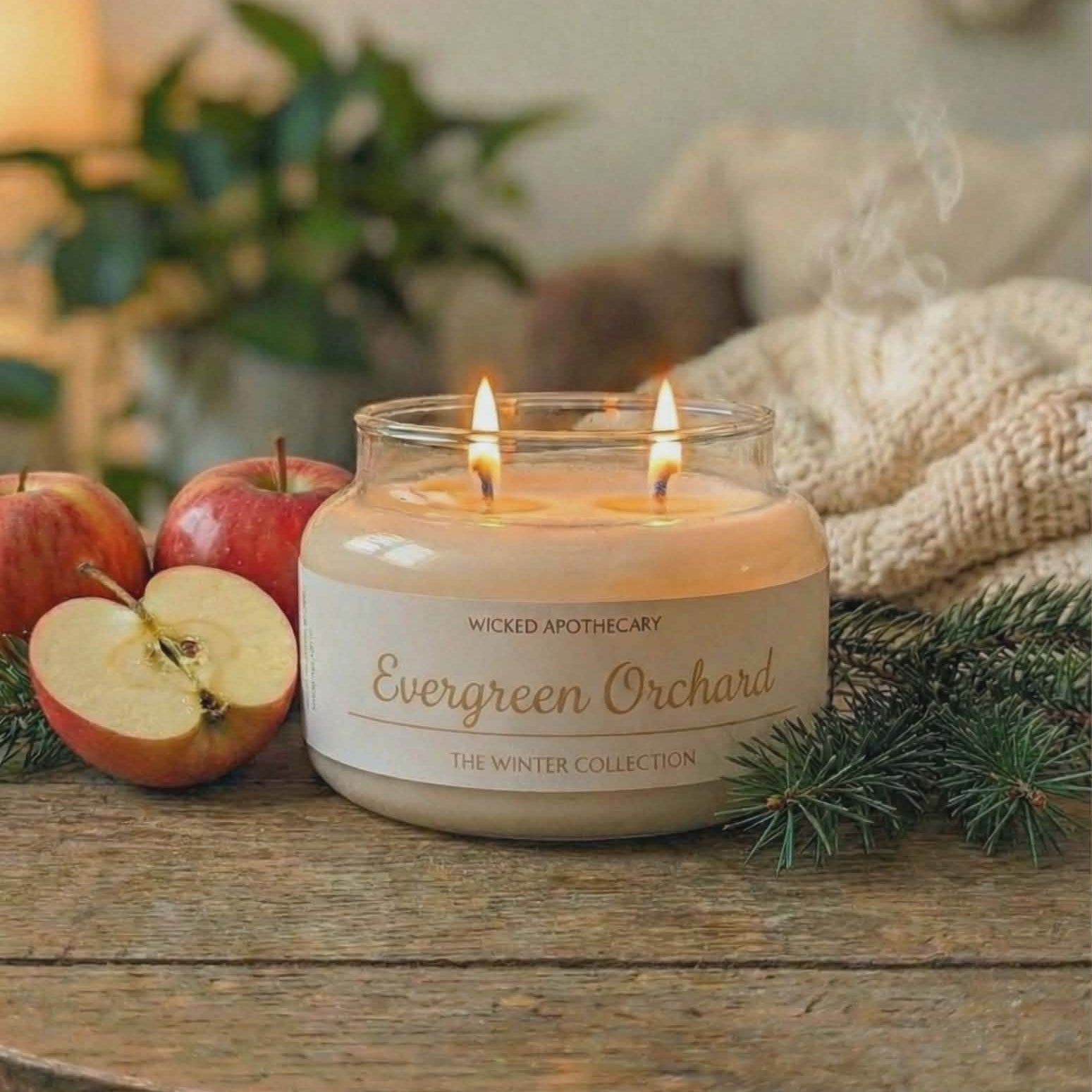 Wicked Apothecary Evergreen Orchard candle on a wooden table with apples and greenery