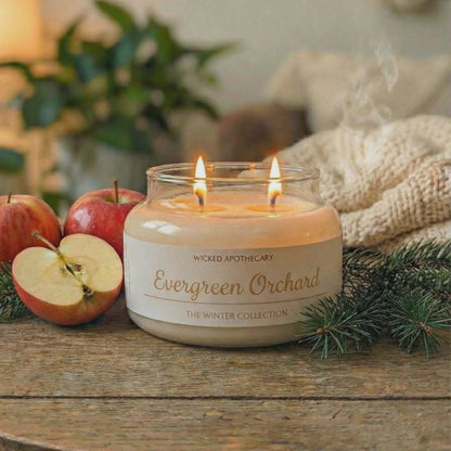 Wicked Apothecary Evergreen Orchard candle on a wooden table with apples and greenery