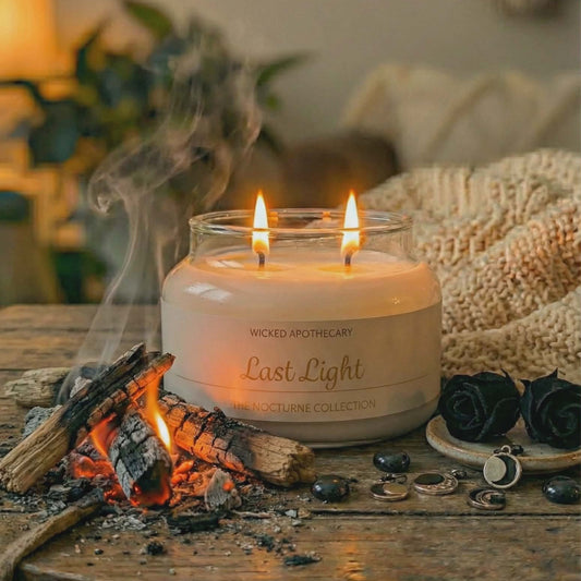Wicked Apothecary 'Last Light' candle on a wooden table with fire and decorative elements.