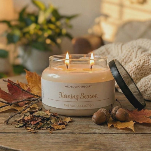 Candle labeled 'Turning Season' on a wooden surface with fall leaves and acorns.