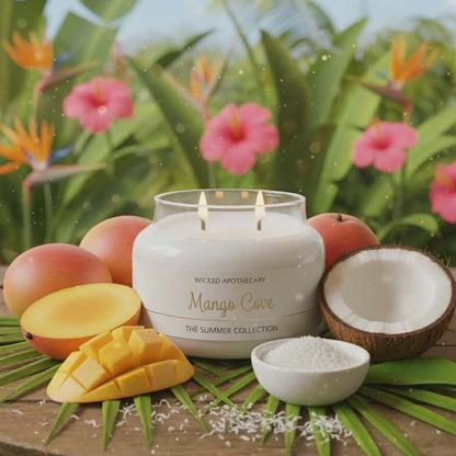 Wicked Apothecary Mango Love candle on a table with mangoes, coconuts, and flowers in the background