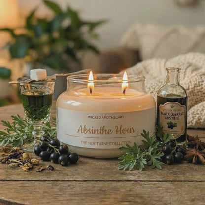 Candle labeled 'Absinthe Hour' from Wicked Apothecary on a wooden table with bottles and greenery.