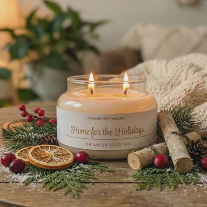 Candle labeled 'Home for the Holidays' from Wicked Apothecary on a wooden table with festive decorations.