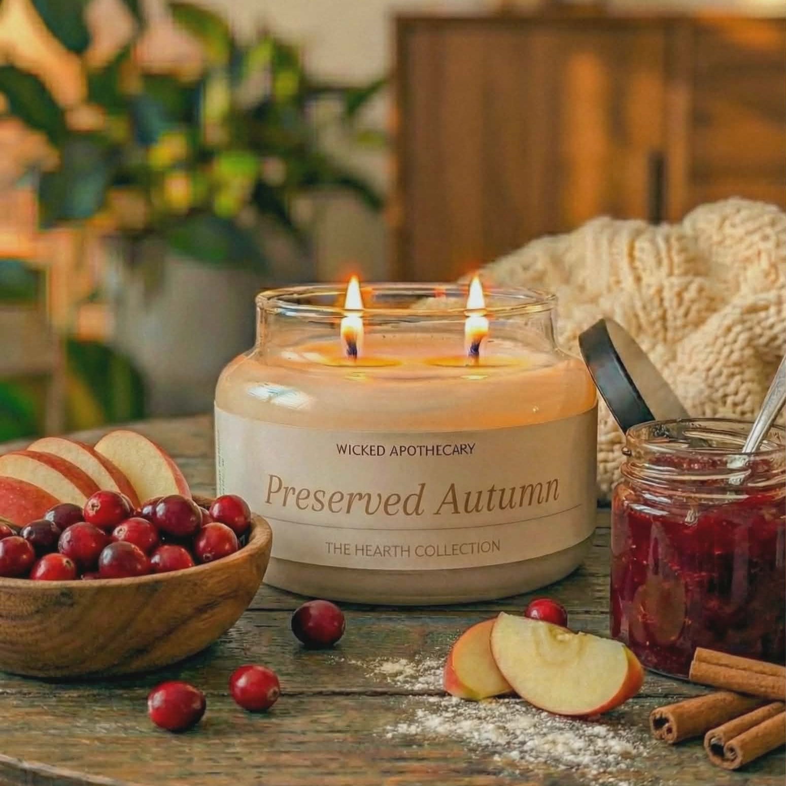 Wicked Apothecary 'Preserved Autumn' candle on a wooden table with apples, cranberries, and cinnamon.