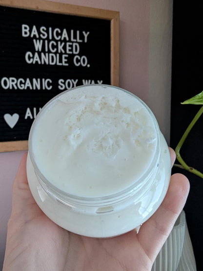 Hand holding a jar of cream with 'Basically Wicked Candle Co.' sign in the background
