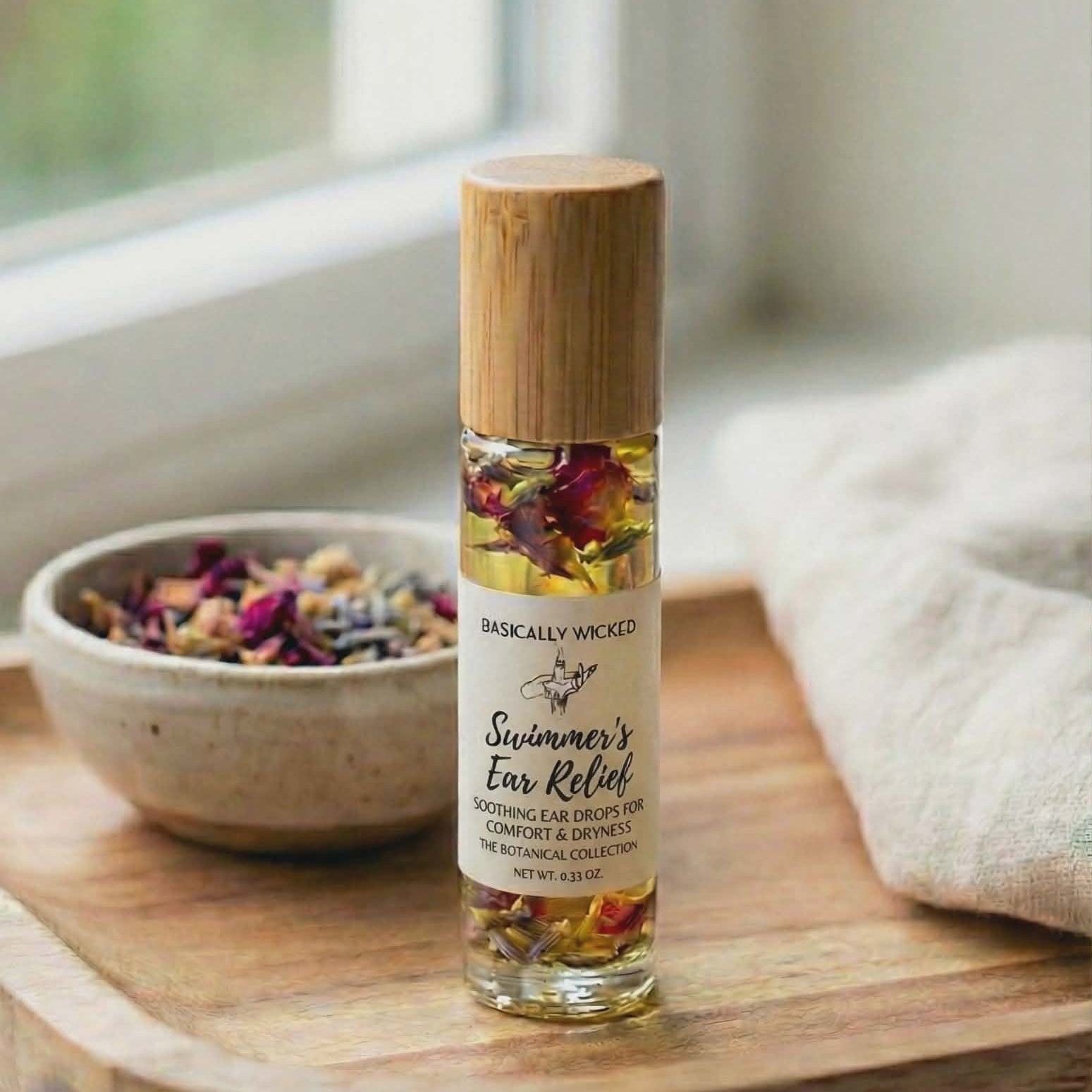 Roll-on bottle with wooden cap on a wooden surface next to a bowl of dried herbs and a towel.