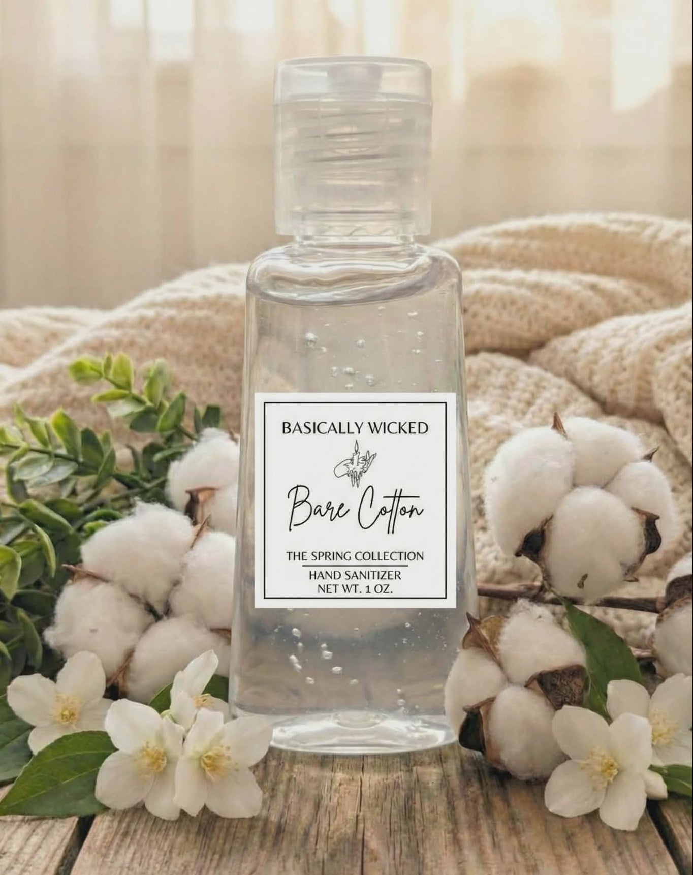 Hand sanitizer bottle labeled 'Basically Wicked' with cotton and flowers on a wooden surface