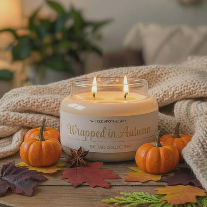 Wicked Apothecary 'Wrapped in Autumn' candle on a wooden table with pumpkins and fall leaves.