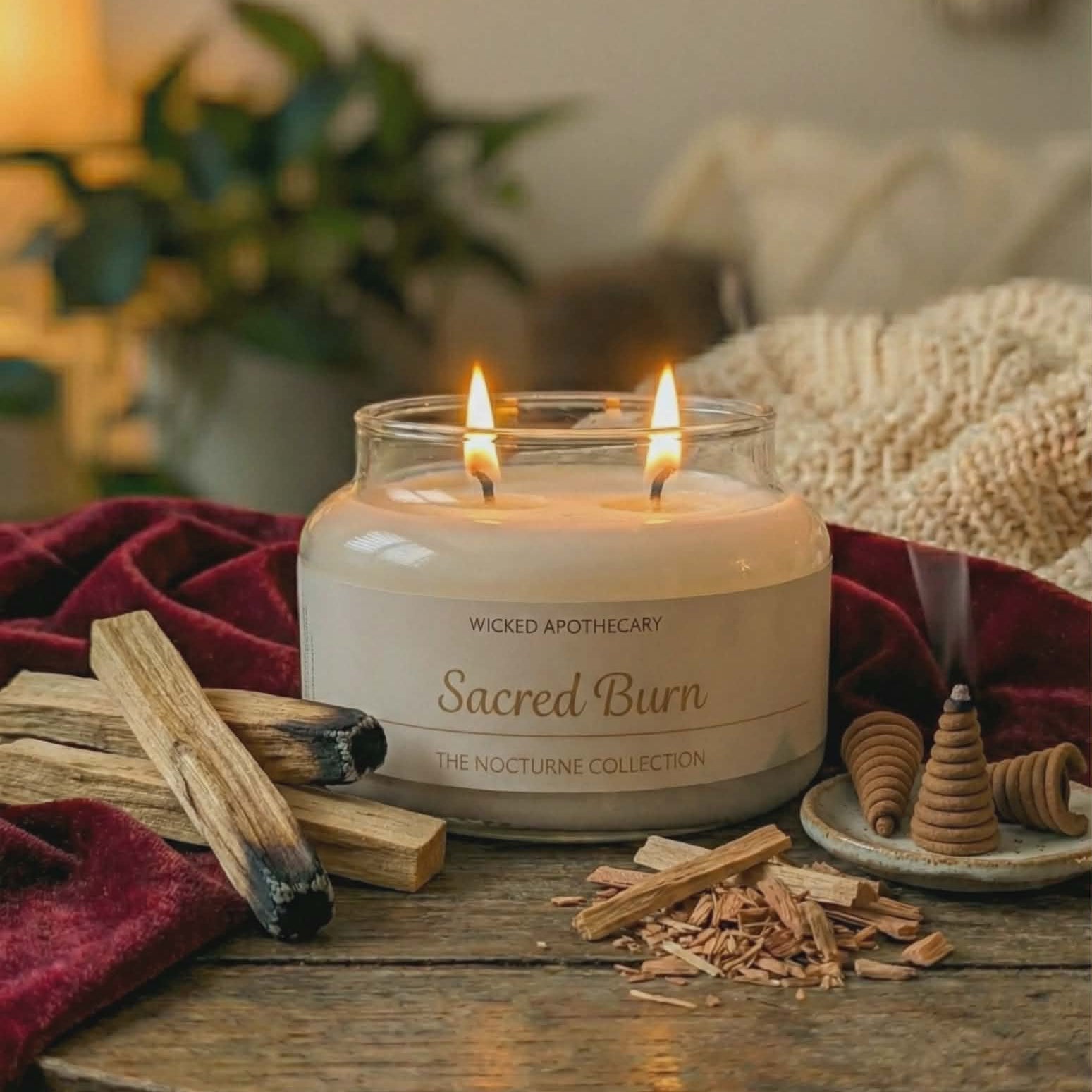 Candle labeled 'Sacred Burn' on a wooden table with wooden sticks and a blurred background