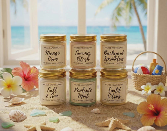 Set of candles with beach-themed packaging on a sandy surface with flowers and a basket in the background.