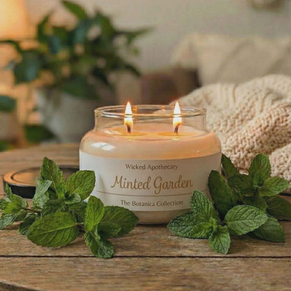 Candle labeled 'Minted Garden' from Wicked Apothecary on a wooden surface with mint leaves.