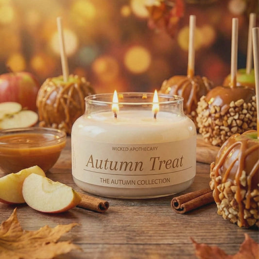 Candle labeled 'Autumn Treat' surrounded by autumn-themed items on a wooden surface.