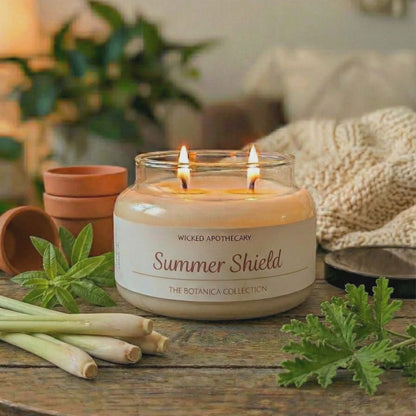 Wicked Apothecary Summer Shield candle on a wooden table with plants and a lamp in the background