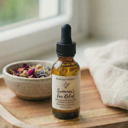 Bottle of 'Swimmer's Ear Relief' on a wooden surface with a bowl of dried herbs in the background.