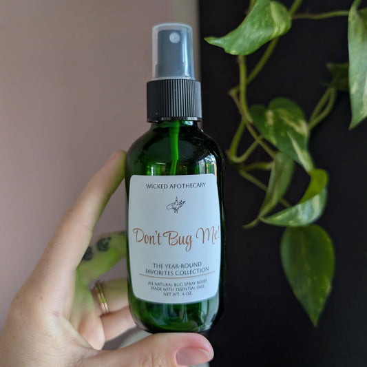 Hand holding a green spray bottle labeled 'Don't Bug Me' with a plant in the background