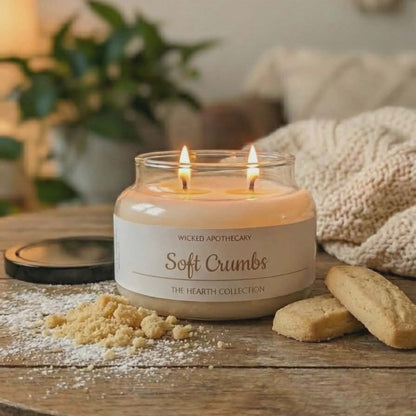 Candle labeled 'Soft Crumbs' from Wicked Apothecary on a wooden table with cookies and a plant in the background.
