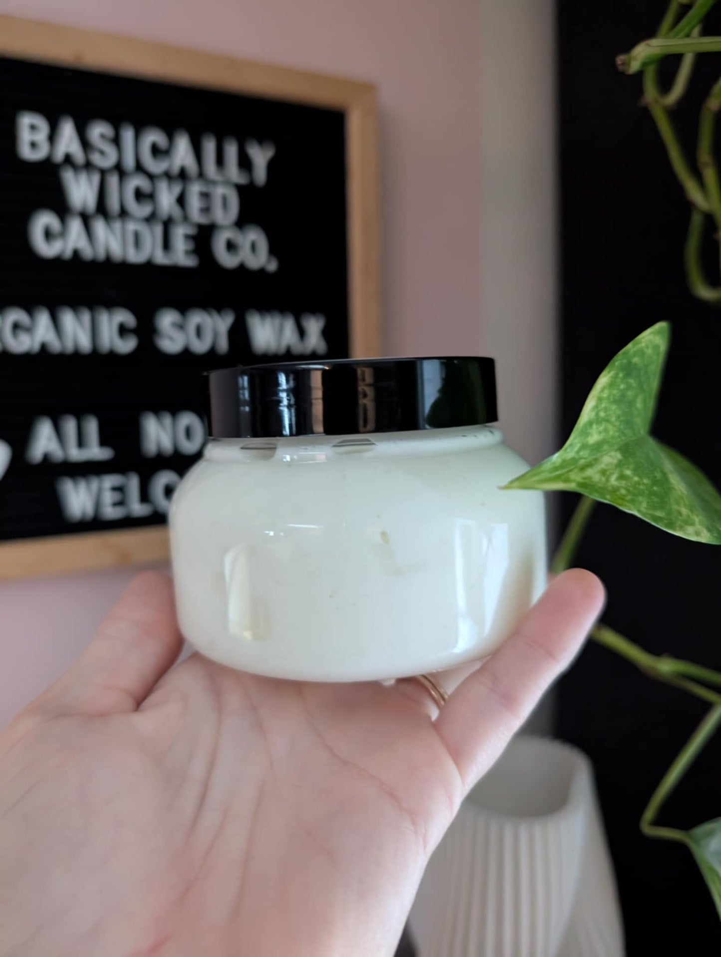 Hand holding a jar of candle with 'Basically Wicked Candle Co.' in the background
