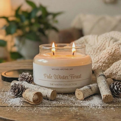Candle labeled 'Pale Winter Forest' from Wicked Apothecary on a wooden table with decorative elements.