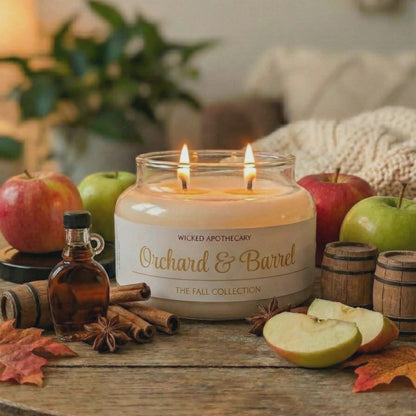 Wicked Apothecary Orchard & Barrel candle on a wooden table with apples, cinnamon, and a bottle of syrup.