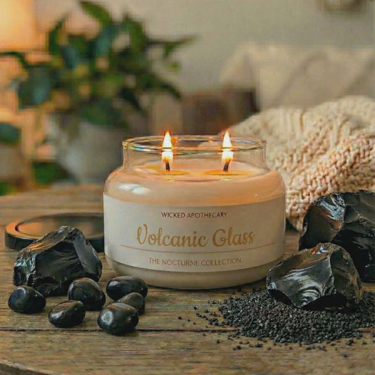 Candle in a glass jar labeled 'Volcanic Glass' on a wooden surface with decorative stones and plants.