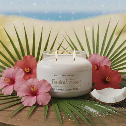 Candle labeled 'Tropical Bloom' with pink flowers and a palm leaf on a decorative surface.