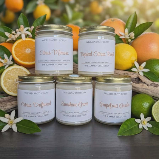 Collection of candles with citrus-themed labels in front of citrus fruits and leaves.