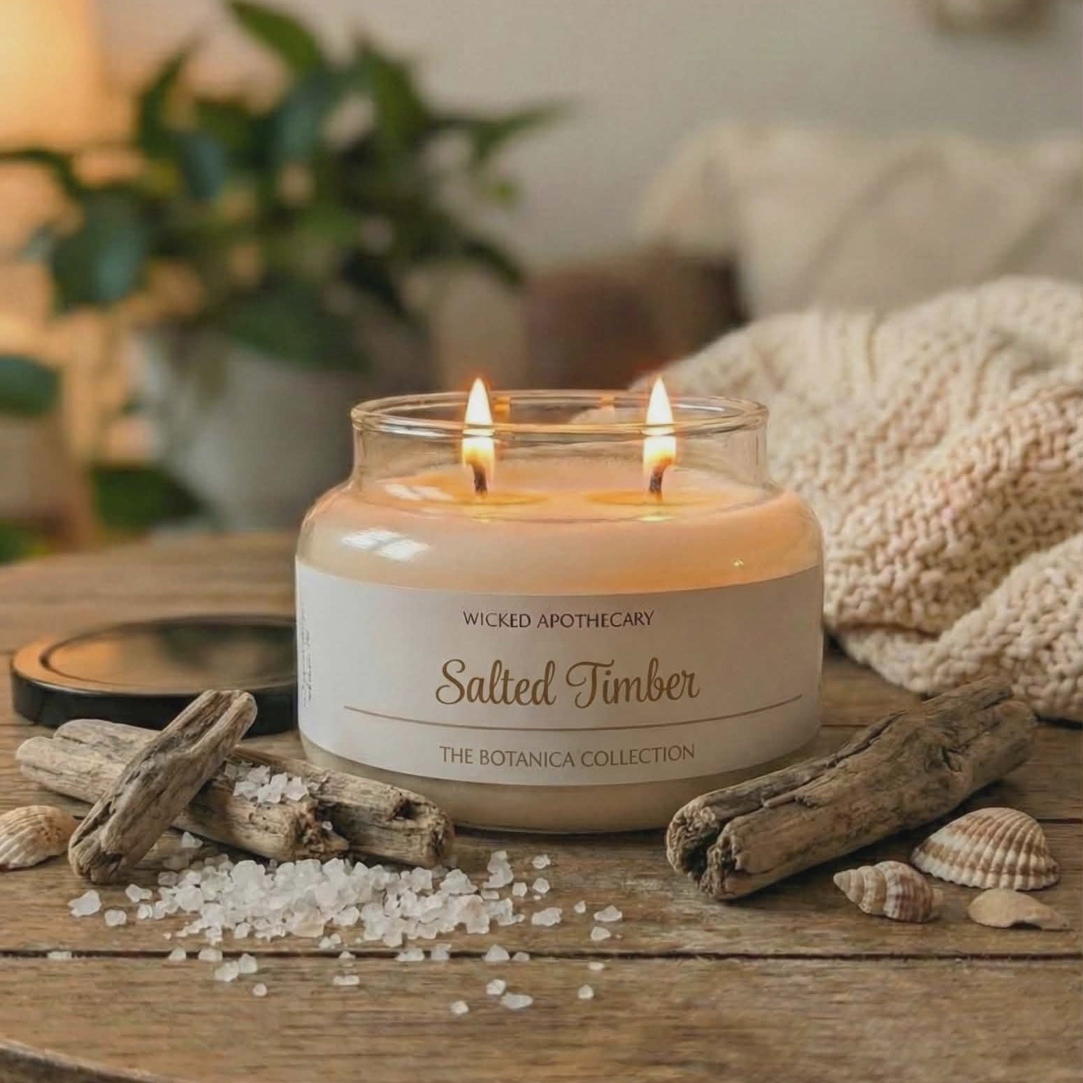 Candle labeled 'Salted Timber' from Wicked Apothecary on a wooden surface with natural elements.