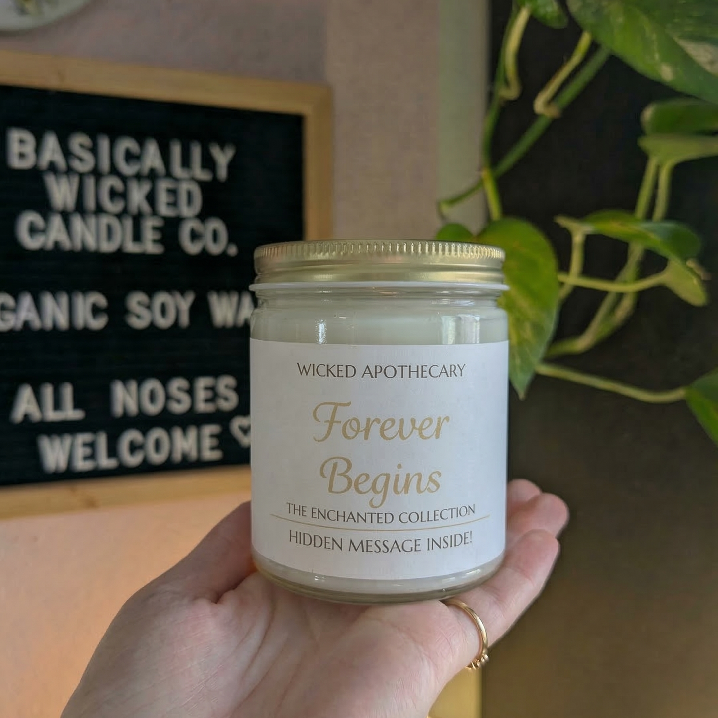 Candle labeled 'Forever Begins' held by a hand with a decorative background