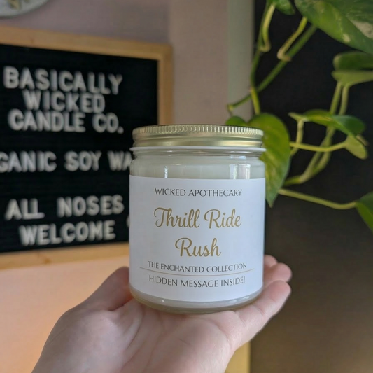 Hand holding a candle labeled 'Thrill Ride Rush' by Wicked Apothecary in front of a sign for Basically Wicked Candle Co.