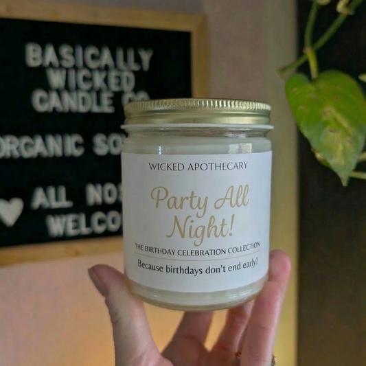 Candle labeled 'Party All Night' by Wicked Apothecary held in front of a store sign.