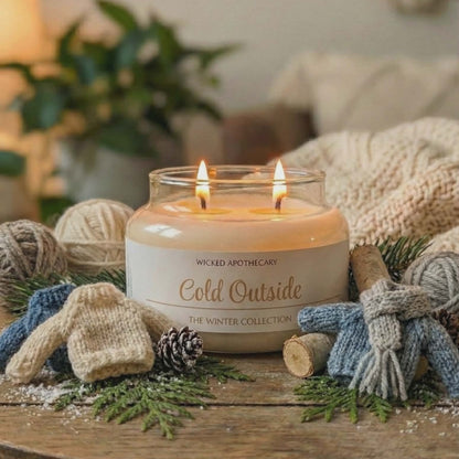 Candle labeled 'Cold Outside' from Wicked Apothecary on a wooden table with winter decor.
