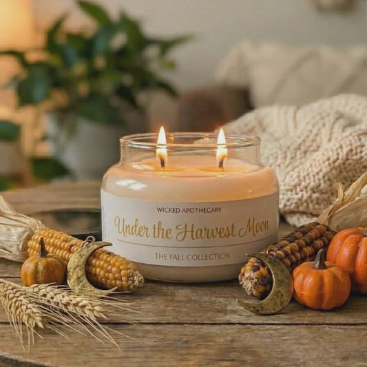 Candle labeled 'Under the Harvest Moon' on a wooden table with fall decorations.