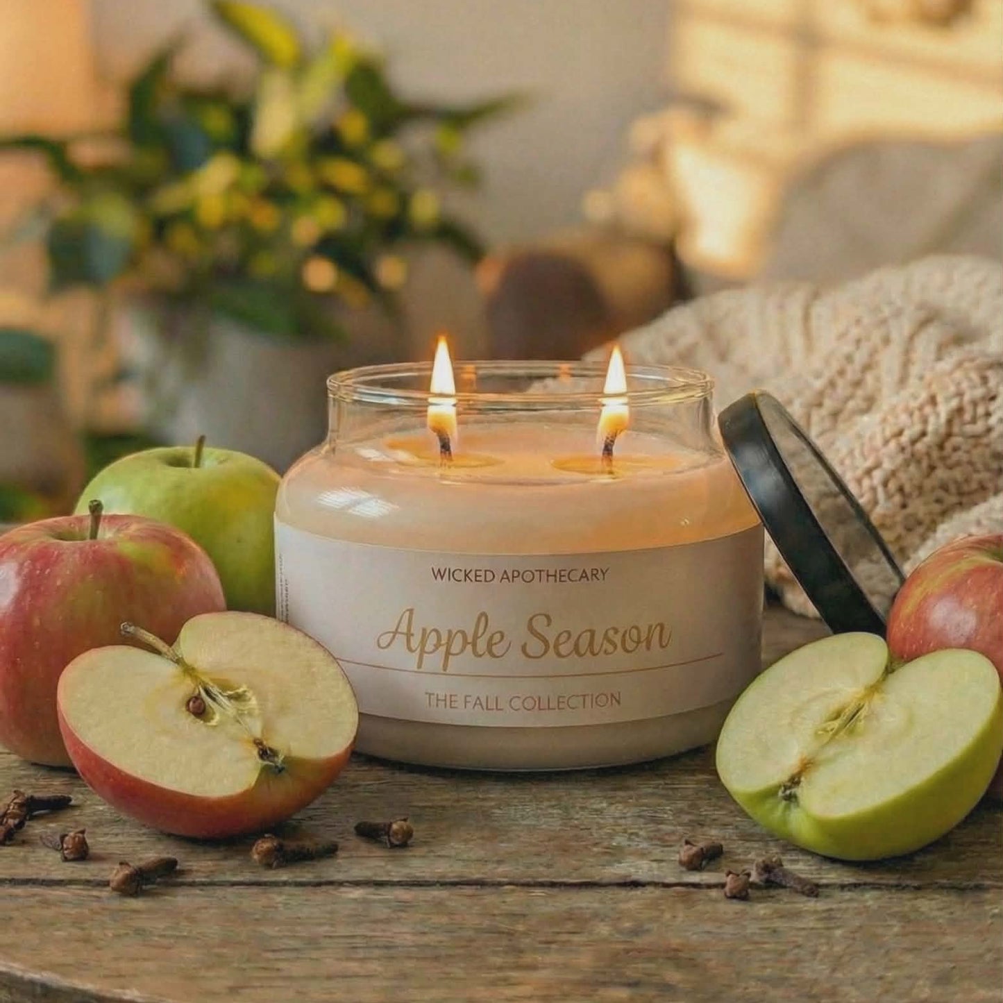 Candle labeled 'Apple Season' on a wooden table with apples and cinnamon sticks.