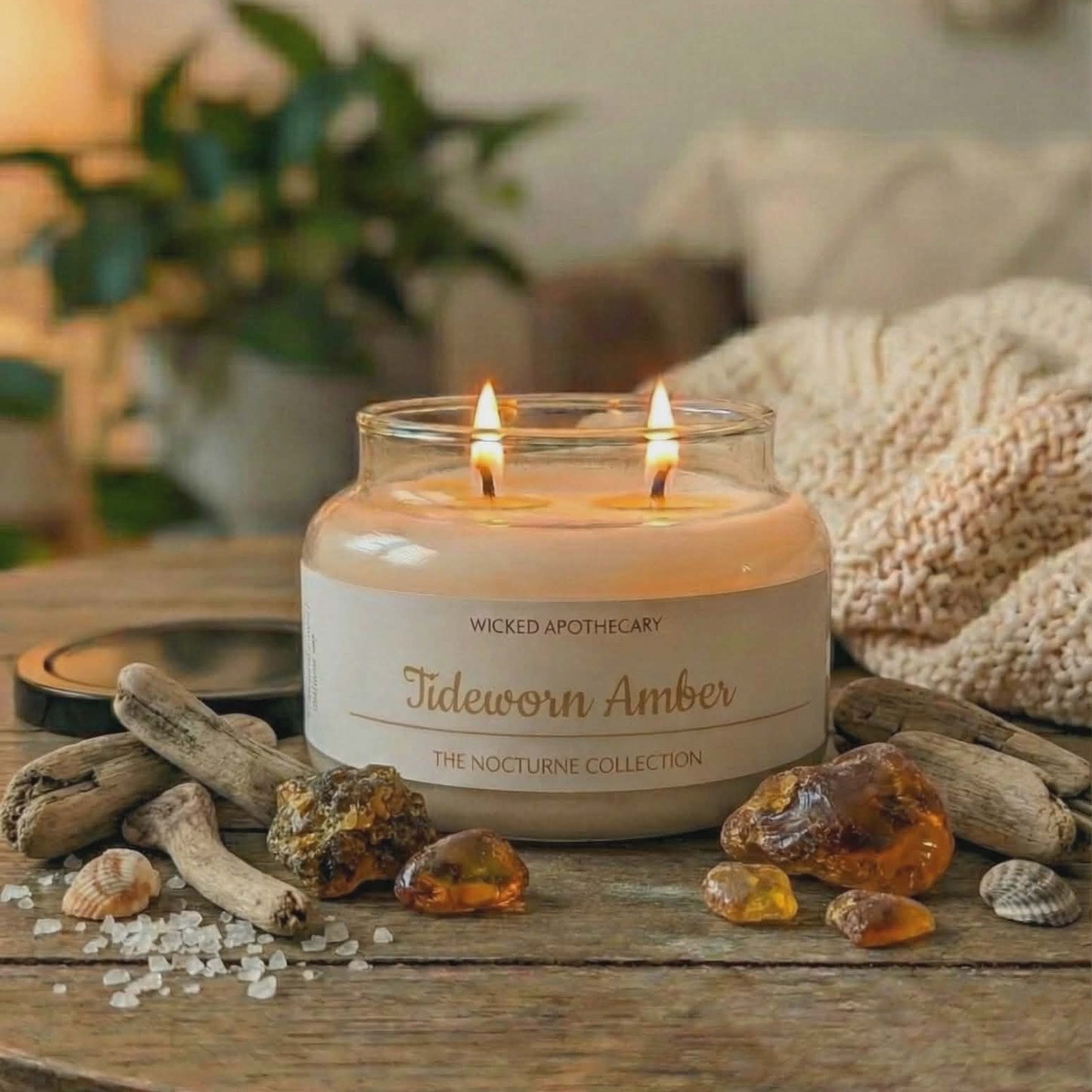 Candle labeled 'Tideworn Amber' from Wicked Apothecary on a wooden surface with amber stones and driftwood.