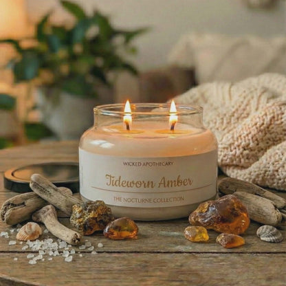 Candle labeled 'Tideworn Amber' from Wicked Apothecary on a wooden surface with amber stones and driftwood.