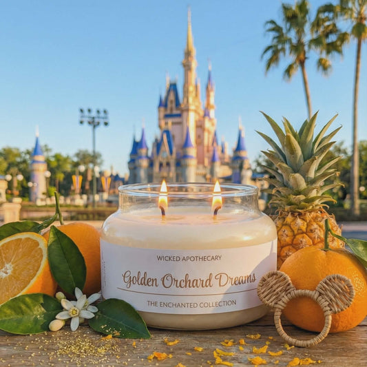 Candle labeled 'Golden Orchard Dreams' with a pineapple, oranges, and leaves on a wooden table with a castle in the background.
