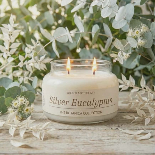 Candle labeled 'Silver Eucalyptus' from Wicked Apothecary on a wooden surface with greenery.