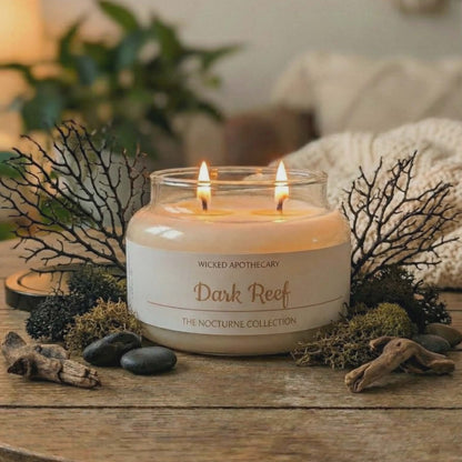 Candle in a glass jar labeled 'Dark Reef' from Wicked Apothecary on a wooden table with decorative elements.