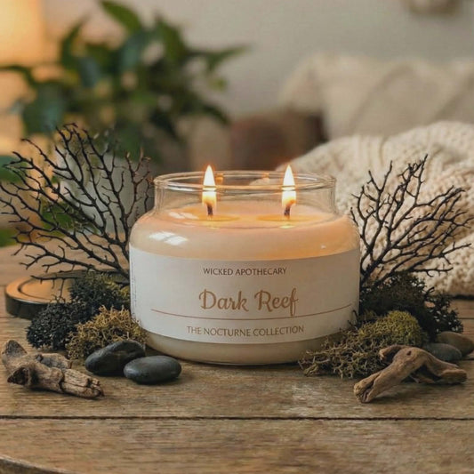 Candle in a glass jar labeled 'Dark Reef' from Wicked Apothecary on a wooden table with decorative elements.