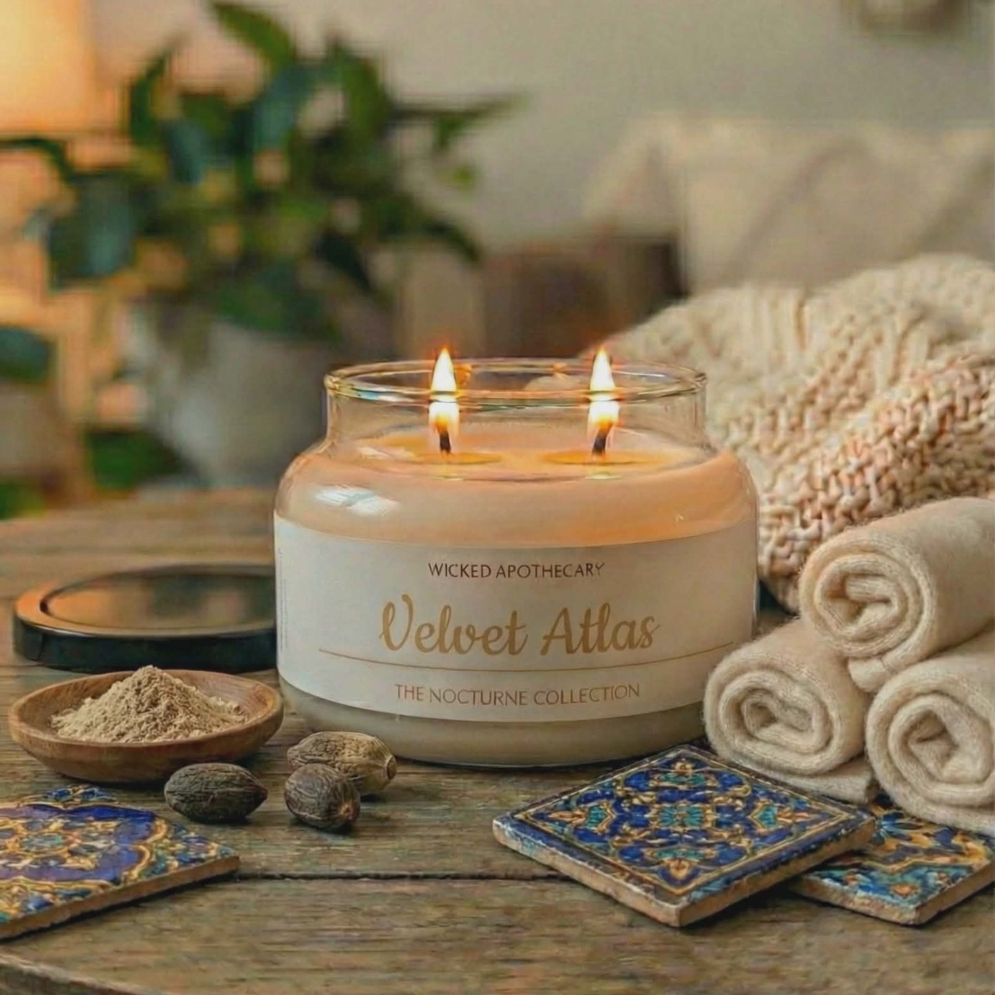 Candle labeled 'Velvet Atlas' on a wooden table with decorative items and plants in the background