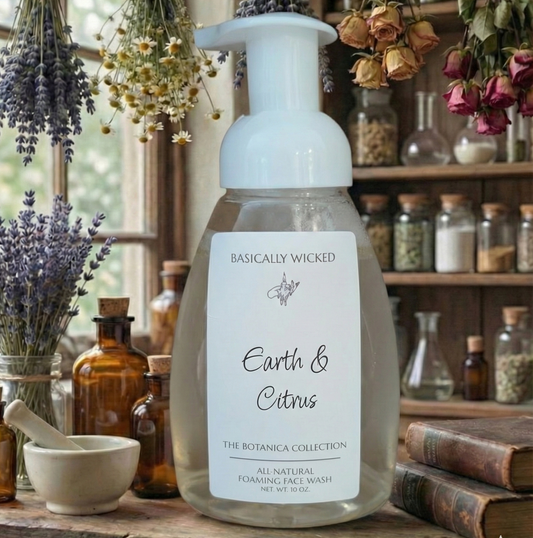 Foaming face wash bottle labeled 'Earth & Citrus' by 'Basically Wicked' on a wooden surface with herbs and bottles in the background.
